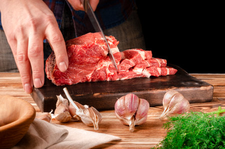 Butcher cutting pork meat on kitchen. The chef cuts the pork meat. On the background of vegetables. On a black background.Butcher shop.Recipes with meatの写真素材