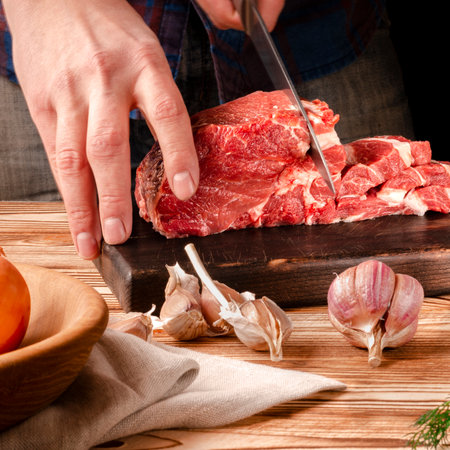 Butcher cutting pork meat on kitchen. The chef cuts the pork meat. On the background of vegetables. On a black background.Butcher shop.Recipes with meatの写真素材