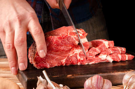 Butcher cutting pork meat on kitchen. The chef cuts the pork meat. On the background of vegetables. On a black background.Butcher shop.Recipes with meatの写真素材