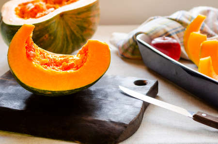 Pumpkin, rustic arrangement with pumpkin cut into pieces, knife, board, wooden spoon, iron pot on a table, with rustic fabricの写真素材