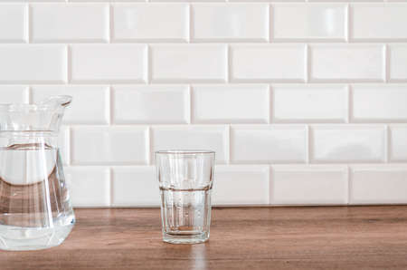 An empty glass and a jug of water stand in the kitchen against a background of white tiles.の写真素材