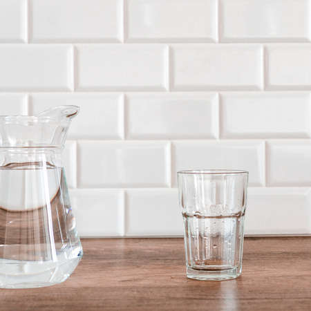 An empty glass and a jug of water stand in the kitchen against a background of white tiles.の写真素材