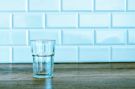 An empty glass water glass stands on a wooden table against a white wall. in the kitchenの写真素材