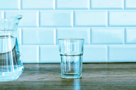 An empty glass and a jug of water stand in the kitchen against a background of white tiles.の写真素材