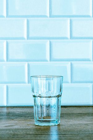 An empty glass water glass stands on a wooden table against a white wall. in the kitchenの写真素材