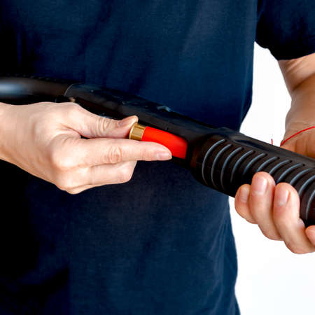 Close up of man loading a red shotgun shell into the magazine of his weapon. Charging a pump smoothbore weaponの写真素材