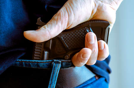 a man in jeans and a t-shirt holds a gun in his hand from the backの写真素材