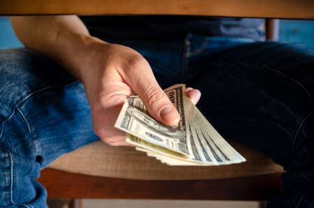 Hands passing money under table corruption bribery, businessman sealing the deal with a handshake and receiving a bribe money.の写真素材