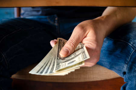 Hands passing money under table corruption bribery, businessman sealing the deal with a handshake and receiving a bribe money.の写真素材