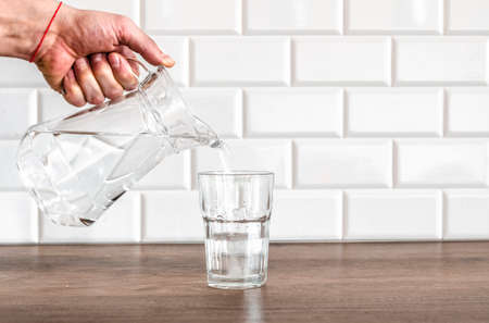 A man's hand pouring fresh pure water from bottle into a glass on the table, health and diet concept, Slow motion footageの写真素材