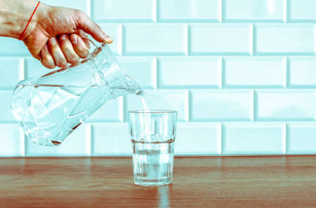 Pouring fresh water from the jug in glass on wooden tableの写真素材