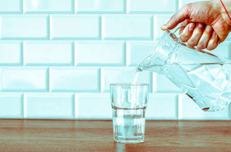 A man's hand pouring fresh pure water from bottle into a glass on the table, health and diet concept, Slow motion footageの写真素材