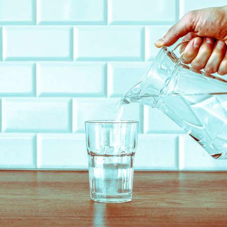Pouring fresh water from the jug in glass on wooden tableの写真素材