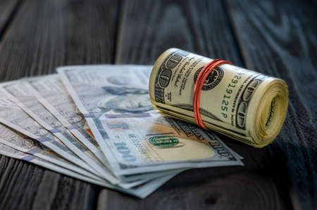 A roll of dollar bills and coins over other bills on a desk. Highlight for the hundred dollar bill.の写真素材