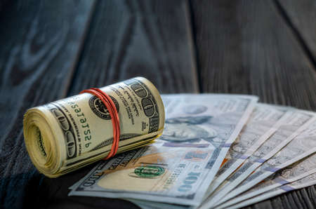 A roll of dollar bills and coins over other bills on a desk. Highlight for the hundred dollar bill.の写真素材