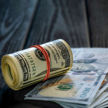 A roll of dollar bills and coins over other bills on a desk. Highlight for the hundred dollar bill.の写真素材