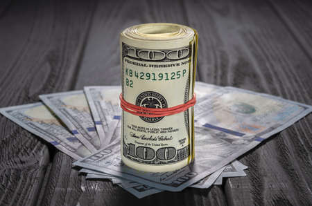 A roll of dollar bills and coins over other bills on a desk. Highlight for the hundred dollar bill.の写真素材