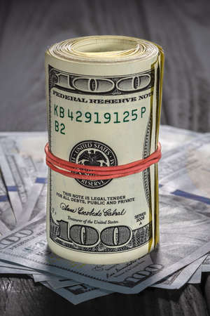 A roll of dollar bills and coins over other bills on a desk. Highlight for the hundred dollar bill.の写真素材