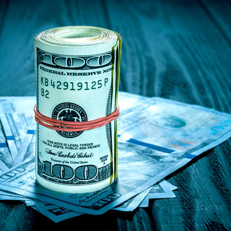 A roll of dollar bills and coins over other bills on a desk. Highlight for the hundred dollar bill.の写真素材