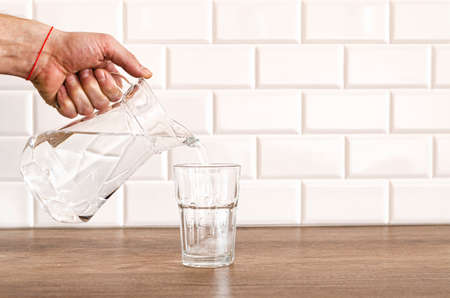 Pouring purified fresh water from the jug in glass on wooden tableの写真素材