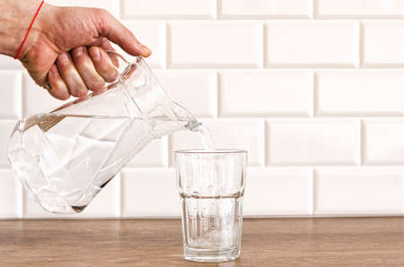 A mans hand pouring fresh pure water from bottle into a glass on the table, health and diet conceptの写真素材