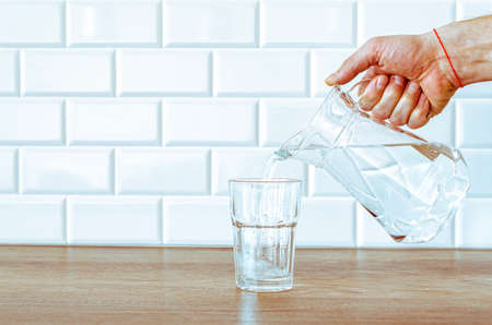 Pouring purified fresh water from the jug in glass on wooden tableの写真素材