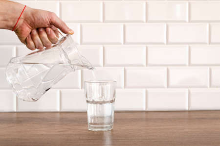 Pouring purified fresh water from the jug in glass on tableの写真素材
