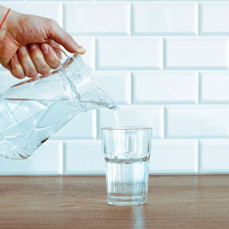 A mans hand pouring fresh pure water from bottle into a glass on the table, health and diet conceptの写真素材