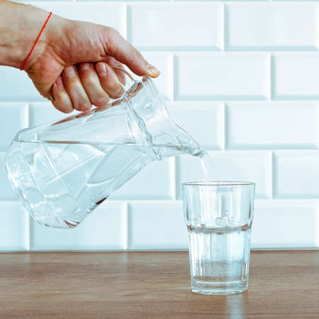 A mans hand pouring fresh pure water from bottle into a glass on the table, health and diet conceptの写真素材