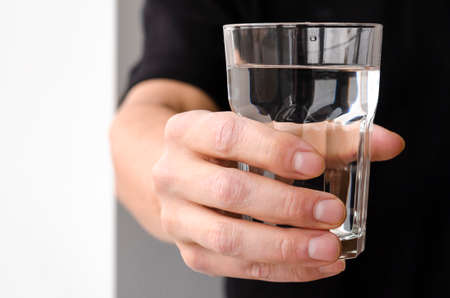 A glass with clean melted water in the hand of a manの写真素材
