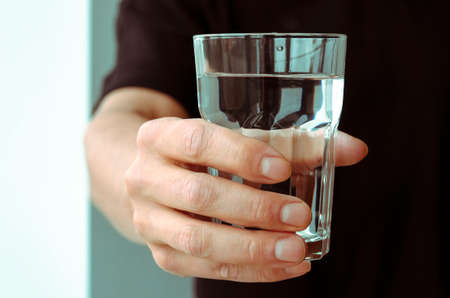 A glass with clean melted water in the hand of a manの写真素材
