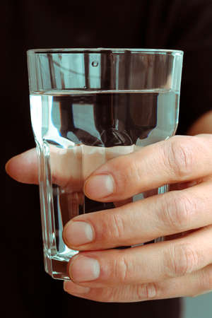 A glass with clean melted water in the hand of a manの写真素材
