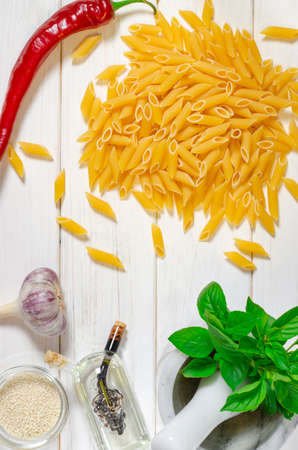 ingredients for italian cousine flat lay. Penne Pasta, green basil, sesame, garlic, chilli lie on a white tree table. View from aboveの写真素材