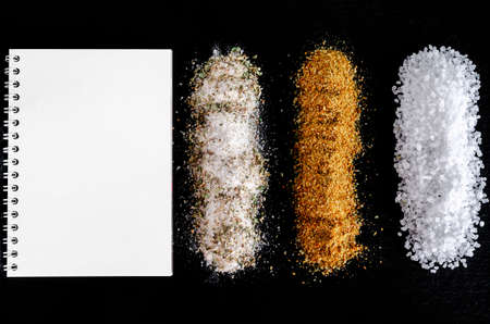 A white notebook, salt and spices lie on a black stoneの写真素材