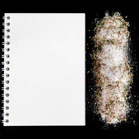 A white notebook, salt and spices lie on a black stoneの写真素材