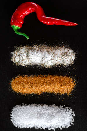Chili peppers, salt, spices, Svan salt and seasonings lie on the black stoneの写真素材