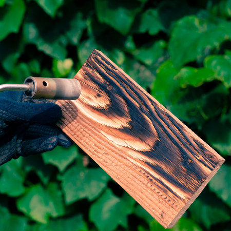 A man burns boards with fire from a gas burner. Wood processing for revealing the beautiful texture of the wood.の写真素材