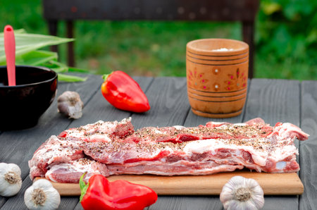 Pork ribs in a marinade lie on a wooden table in the garden next to pepper, garlic, corn on the grill background. Ready to eatの写真素材