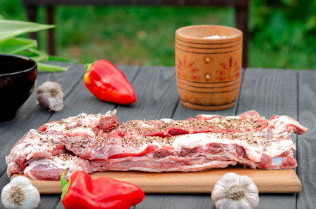 Pork ribs in a marinade lie on a wooden table in the garden next to pepper, garlic, corn on the grill background. Ready to eatの写真素材
