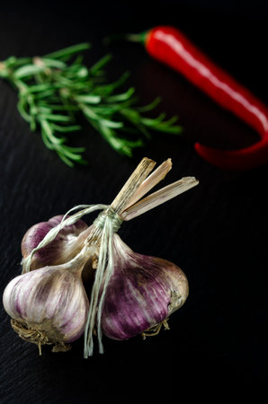 Spices for cooking. A bunch of garlic on a black background next to the rormarin and chili peppersの写真素材