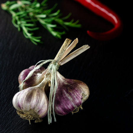 Spices for cooking. A bunch of garlic on a black background next to the rormarin and chili peppersの写真素材
