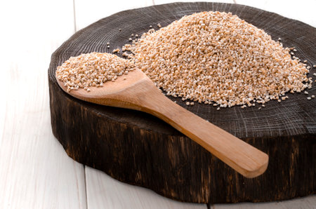 A healthy way of life. Coarse barley grits on a round wooden boardの写真素材