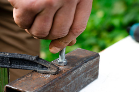 Working with metal. A mans hand screws a bolt into a metal nutの写真素材