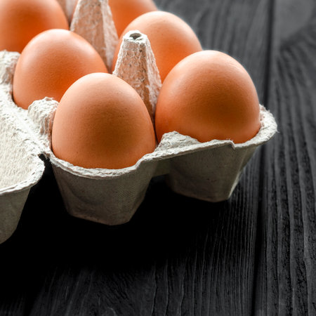 Brown eggs in carton box on a black wooden tableの写真素材