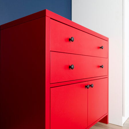 New red chest of drawers in the interior of the apartment against the background of a blue wall and a white wardrobeの写真素材