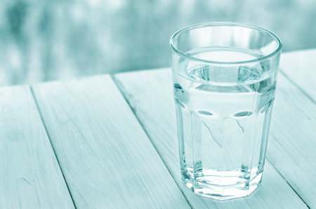 A glass of pure spring water stands on a white wooden backgroundの写真素材