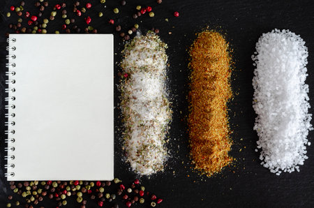 A white notebook, salt and spices lie on a black stone. kitchen backgroundの写真素材