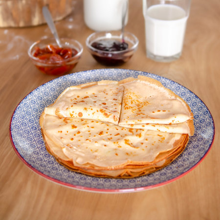 Sweet round pancakes lying on a round plate next to jamの写真素材