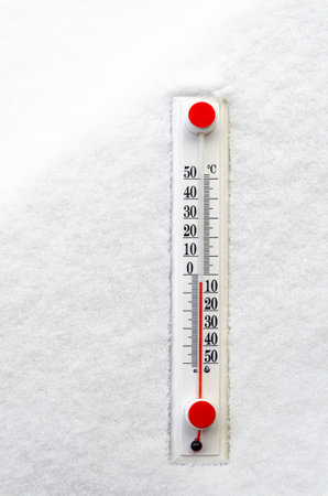 Temperature A white thermometer with a red scale lies on white snow. Winter.