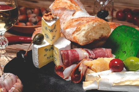Cheese and cold cuts, olives and baguette on a wooden board. Cold appetizersの写真素材